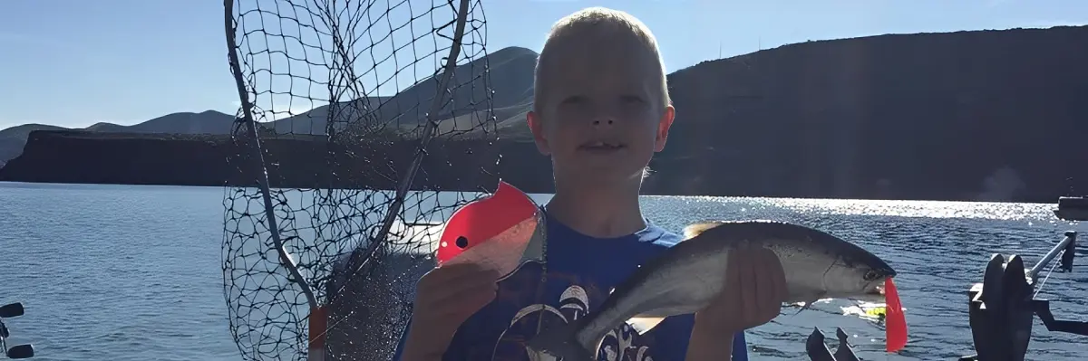Child holding fish and lure by lake.