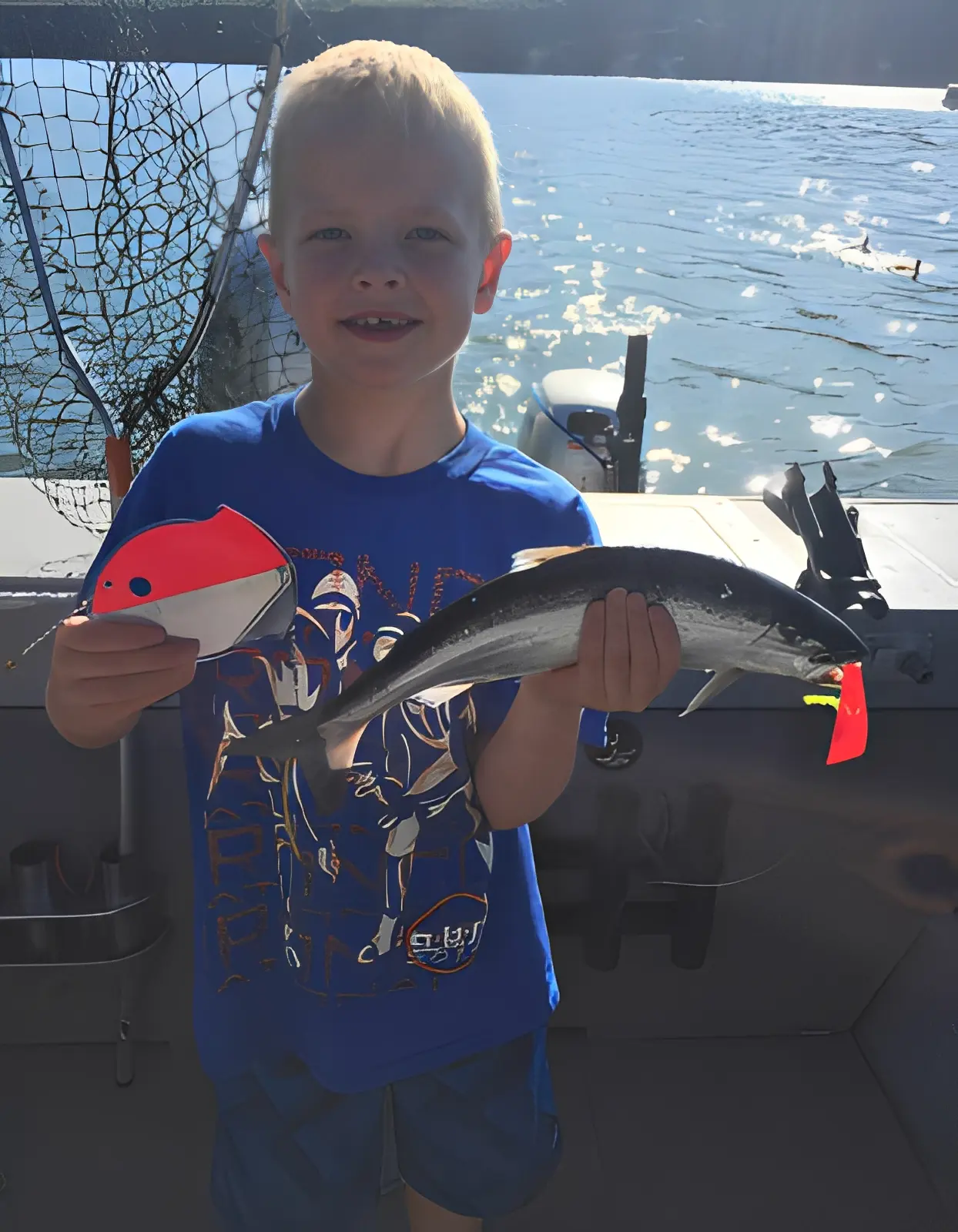 Child holding fish and fishing lure on boat.