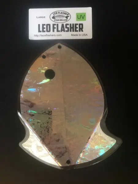 Shiny fish-shaped LED flasher with holographic surface against dark background.