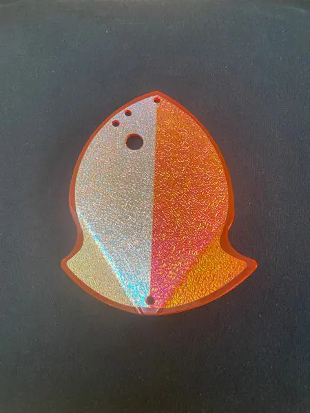 A colorful, fish-shaped glittery object with two holes on top.