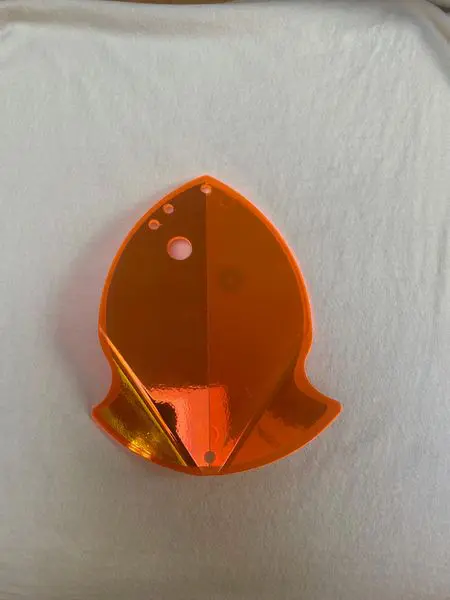 Orange reflective marker shaped like a fish on a white surface.