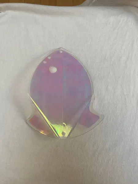 A shiny, translucent, iridescent fish-shaped object on a white surface.