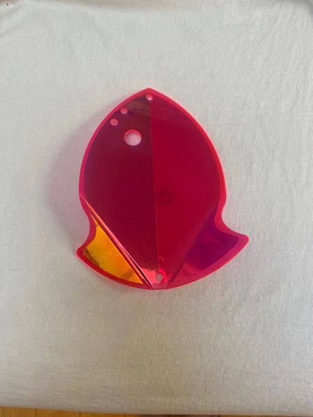 A small pink and orange plastic fish-shaped object on a white surface.